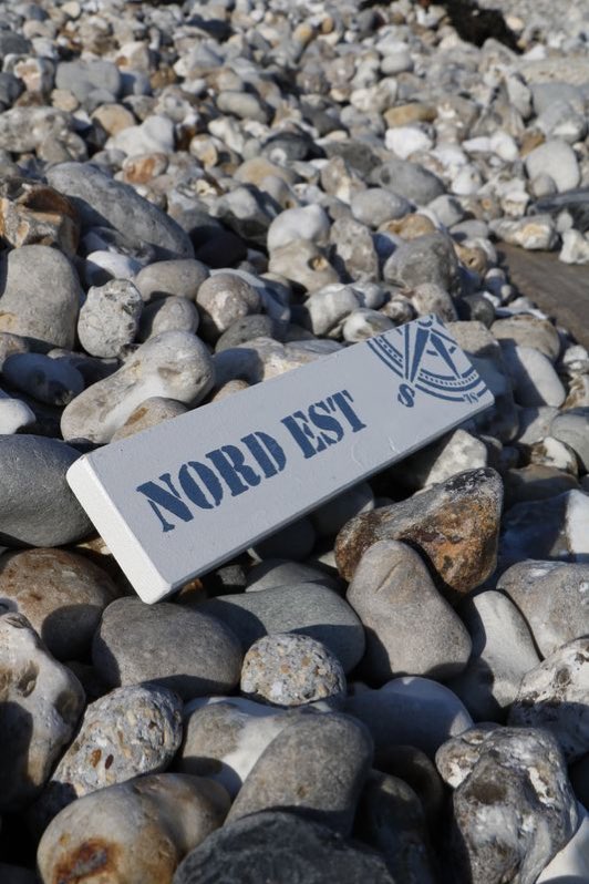 Pancarte en bois « Nord Est » posée sur des galets.