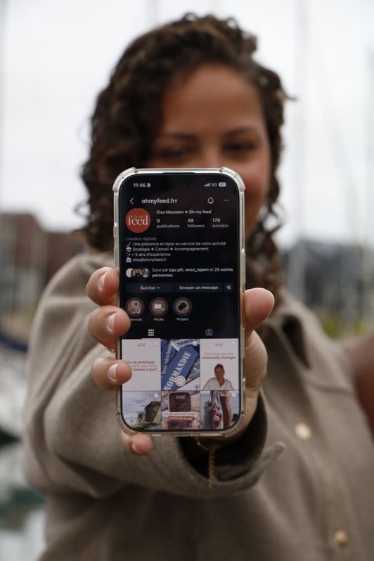 Smartphone tendu vers l'objectif, affichant un profil Instagram.