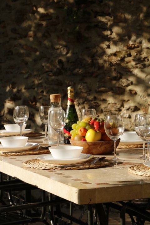 Table dressée en extérieur, avec vaisselle, fruits et bouteilles.