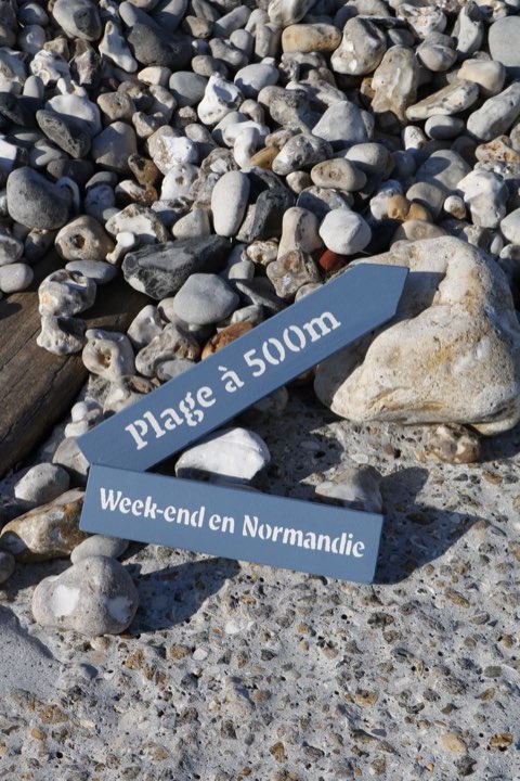 Pancartes en bois « Plage à 500 m » posées sur des galets.