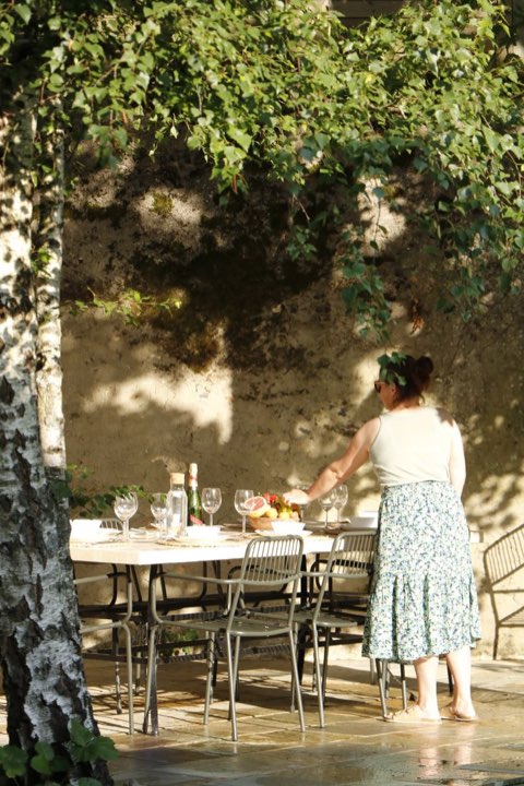 Femme dressant une table de jardin à l'ombre d'une treille.